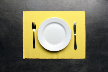 Empty plate, cutlery and yellow placemat on dinning table