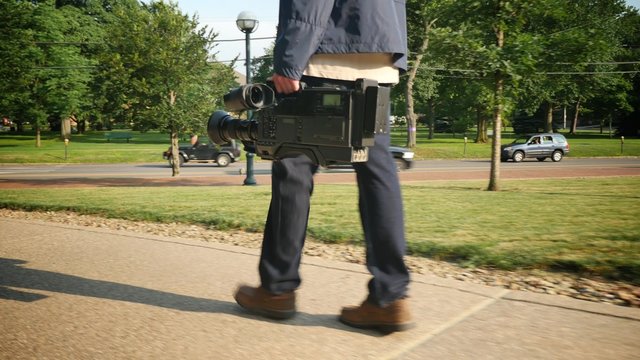 Walking Beside Cameraman Carrying Video Camera