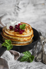 pancakes with honey, sour cream and red currants in a vintage scourage on a light wooden background