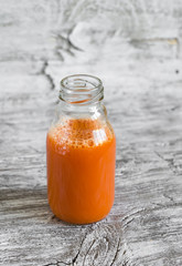 fresh carrot juice in a glass bottle on a light wooden background