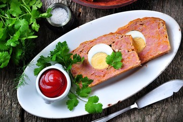 meat loaf with boiled egg, tomato sauce, coriander and parsley on a wooden table. rustic style.