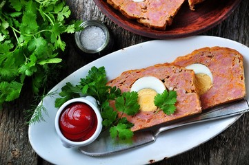meat loaf with boiled egg, tomato sauce, coriander and parsley on a wooden table. rustic style.