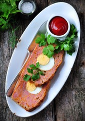 meat loaf with boiled egg, tomato sauce, coriander and parsley on a wooden table. rustic style.