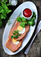 meat loaf with boiled egg, tomato sauce, coriander and parsley on a wooden table. rustic style.