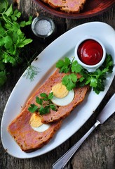 meat loaf with boiled egg, tomato sauce, coriander and parsley on a wooden table. rustic style.