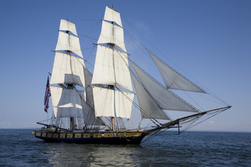 Obraz na płótnie Canvas Tall ship with American flag sailing on blue waters