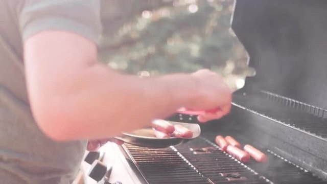 A man taking hot dogs off the grill