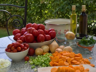 Vegetables, tomatoes, onions, chopped celery, carrot and basil leaves on the table with bottles of olive oil and balsamico vinegar. Preserving jars, cooking pot. Cooking of italian style tomato sauce.