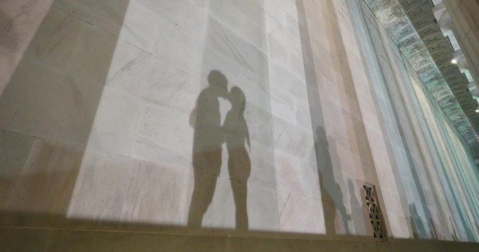 Two lovers kiss at the base of the Lincoln Memorial at night while their shadows fall on the marble walls.