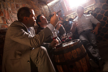 Three businessmen sitting in the wine cellar drinking wine and smoke cigar, resting after a hard day at work.