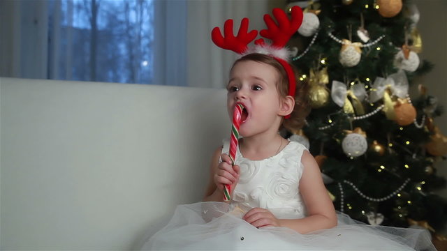 Little cute girl eating a piece of candy on the eve of Christmas.