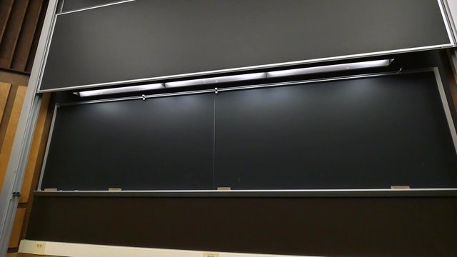 A large chalkboard lowers into place in front of a university's classroom.
