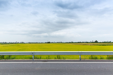 Asphalt road in urban of Thailand with rice green field background.
