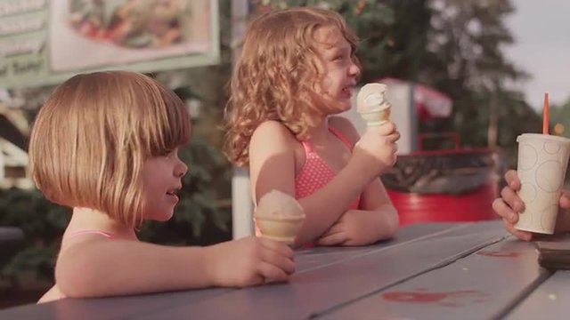 Two sisters eating ice cream with their family at a picnic table