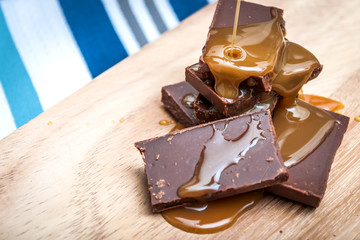 Chocolate pieces stacked on a wooden table and a kitchen towel that gives the image a rustic feeling.