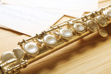 Obraz premium Silver flute with music notes on wooden table close up