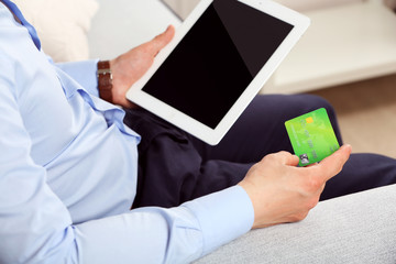 Man holding credit card and tablet on sofa in room