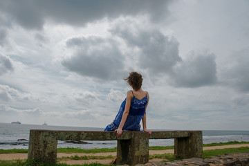 Woman look into distance sitting on bench near sea