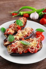 Dish of eggplant with cherry tomatoes and cheese in white plate on wooden table, closeup