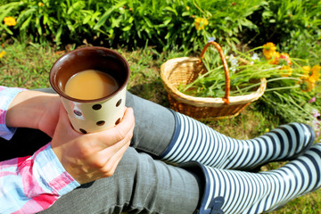 Young woman with cup of coffee sitting on meadow outdoors