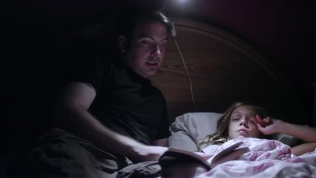 A father reading his daugher a book before bed
