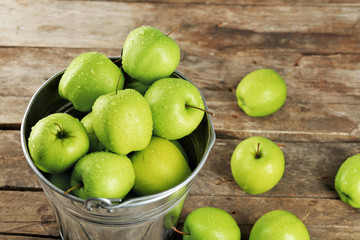 Ripe green apple in metal bucket on wooden table close up