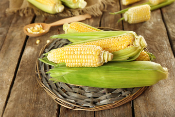 Fresh corn on cobs on wicker mat on wooden table, closeup