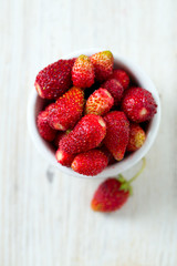 wild strawberries in a bowl on wooden surface