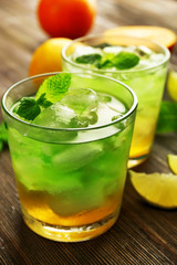 Glasses of lime juice with orange on wooden table, closeup