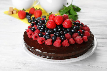 Delicious chocolate cake with summer berries on white wooden background