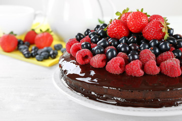 Delicious chocolate cake with summer berries on white wooden background