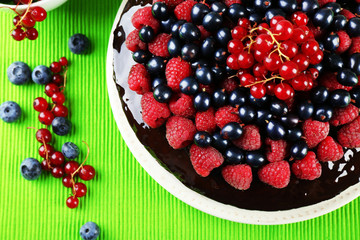 Delicious chocolate cake with summer berries on green tablecloth, top view