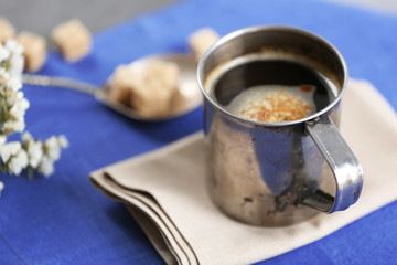 Metal cup of flavored coffee with lump sugar and flowers on table with napkin, closeup