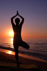 Young healthy woman practicing yoga on the beach at sunset