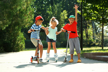 Fototapeta premium Children riding on scooters and roller skates in park