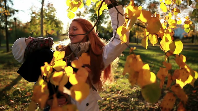 Young mother and daughter admire the yellow leaves in autumn park.