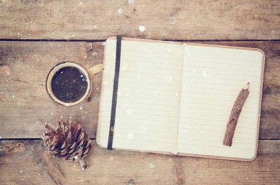 top image of open notebook with blank pages, next to pine cones and cup of coffee over wooden table. top image, glitter overly
