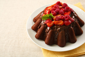 Tasty chocolate muffin with glaze and berries on table close up