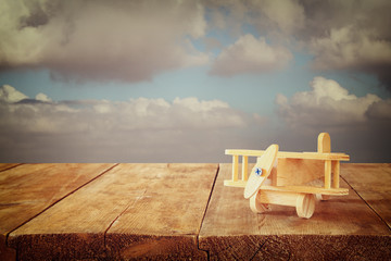 image of wooden toy airplane over wooden table against cloudy sky. retro style image
