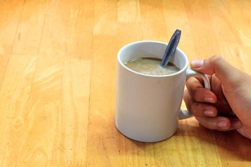 hand someone holding cup of coffee,spoon and blur wood backgroun