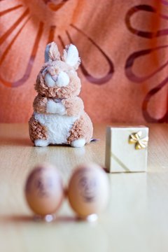 Painted easter eggs with man and woman smiling faces. Eggs on wedding rings. Blurred background with golden gift box and easter bunny. Conceptual funny image. Focus on toy