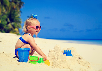 cute little girl building sandcastle on beach