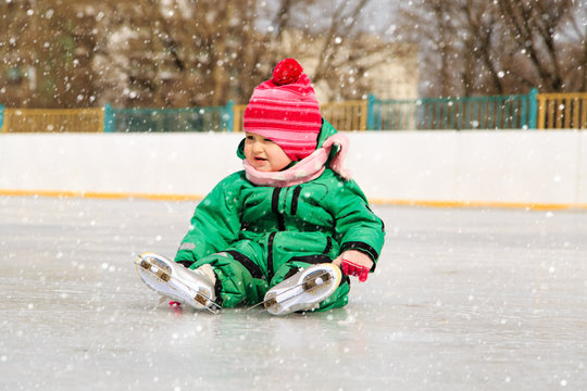 little girl sitting on ice with skates after the fall