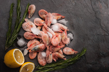 Frozen shrimps  with lemon and rosemary on the black stone table
