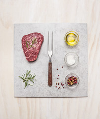Raw fresh meat Steak with spice ingredients on light marble plate over wooden background, top view