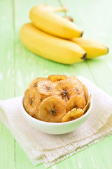 Banana chips in bowl and fresh bananas