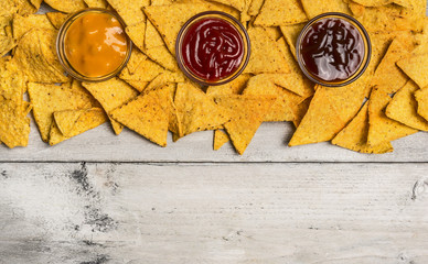 Mexican nacho chips and colorful dip in glass bowls on white wooden background, top view, horizontal border