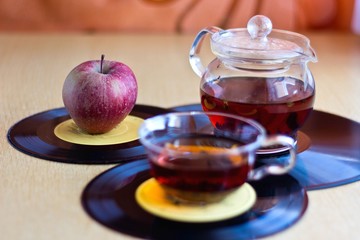 Morning musical tea in glass cup and teapot with ripe apple on vinyl records. Blurred background, focus on apple