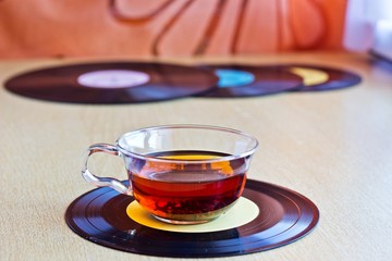 Strong black tea in glass cup on vinyl record discs. Selective focus on cup, close up