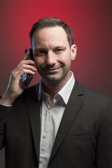 Naklejka premium likeable man in jacket using smartphone in front of red background